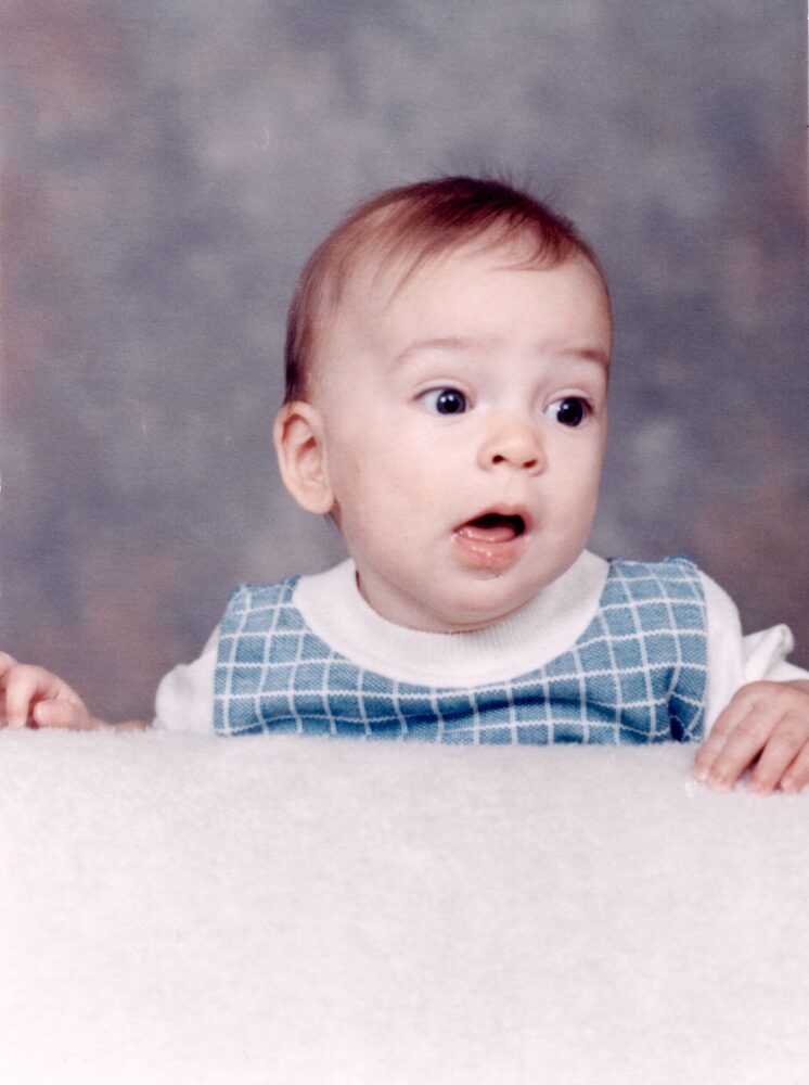 Baby Jake in a blue gingham outfit, peering over the edge of a portrait backdrop